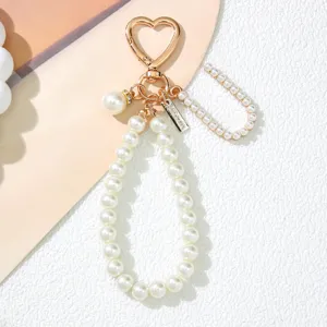 Close-up of elegant pearl keychain with golden heart clasp and engraved metal tag detail