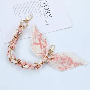 Macro view of pink floral silk scarf interwoven with elegant gold metal phone chain