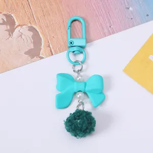 Detail view of a cute turquoise resin bow keychain featuring pearls and a fuzzy green pom-pom