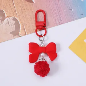 Close-up of a cute red resin bow keychain with white pearls and a soft red pom-pom.