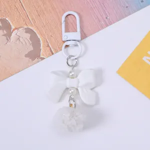 Detailed view of cute white resin bow keychain with faux pearls and soft fluffy pom-pom
