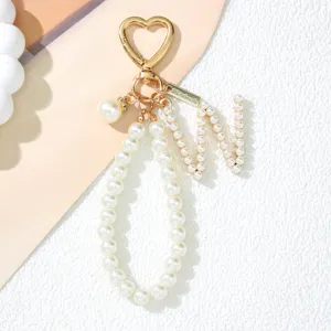 Close-up detail view of pearl letter M keychain with gold heart clasp and handmade tag