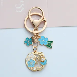 Gold floral wreath keychain with blue enamel cherry blossoms and delicate pearl accents