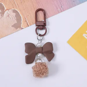 Close-up detail of cute brown resin bow keychain with pearls and soft fuzzy pom-pom pendant