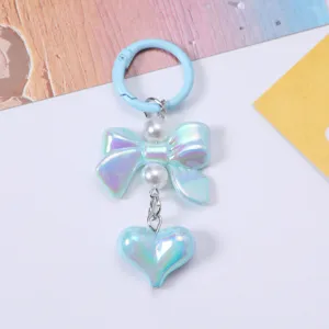 Detail view of an iridescent light blue bow and heart-shaped bag charm with pearls.
