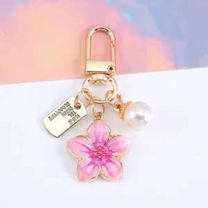 Dettaglio del ciondolo smaltato a fiore di ciliegio rosa con perla e targhetta in metallo