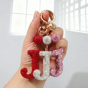 Vue détaillée de trois porte-clés lettre J en strass de couleurs rouge, argent et rose