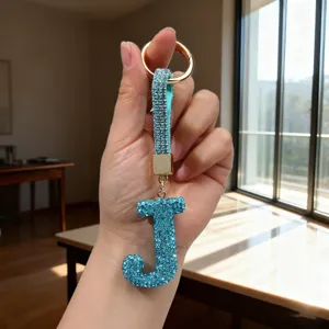Close-up of a sparkling teal rhinestone 'J' letter keychain charm with a gold ring
