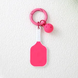 Détail d'un porte-clés rose avec raquette et balle de pickleball sur fond blanc