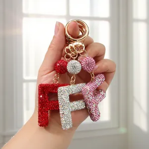 Main tenant des porte-clés étincelants en strass lettre F en rouge, argent et rose