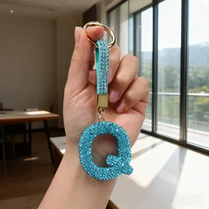 Detail view of a sparkling blue rhinestone letter Q keychain held by hand.