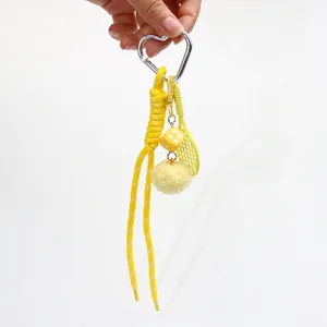 Close-up of yellow tennis racket and dice charm keychain with heart carabiner