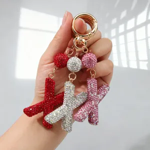 Détail de porte-clés en forme de lettre 'X' sertis de strass étincelants en plusieurs couleurs.