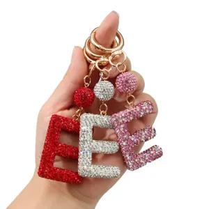 Porte-clés étincelants en strass avec la lettre E en rouge, argent et rose tenus à la main