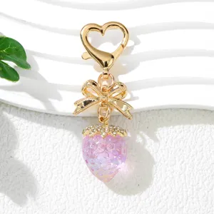 Close-up of cute pink UV strawberry keychain with gold bow and heart clasp