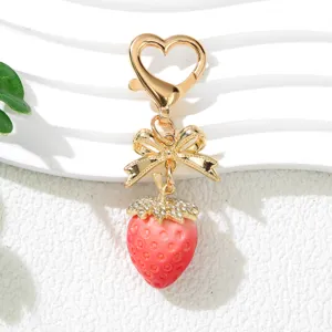 Close-up view of cute pink strawberry keychain featuring a gold bow and rhinestone details.