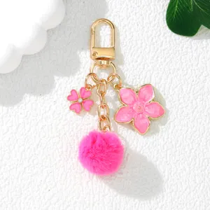 Detailed view of a pink sakura enamel flower and soft faux fur pom-pom keychain charm