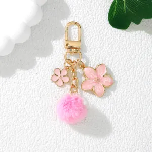 Close-up detail of a pink cherry blossom keychain with fluffy pom-pom and gold hardware
