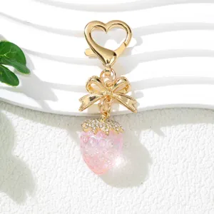 Detailed close-up view of a pink UV strawberry keychain with a golden bow charm.