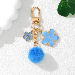 Macro view of blue Sakura flower keychain featuring a soft fur ball and gold clasp.