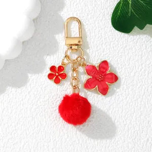 Detailed view of a red cherry blossom and pom-pom keychain with gold-tone hardware