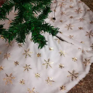 Close-up detail of white plush Christmas tree skirt with elegant gold sequin snowflakes
