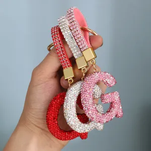Close-up detail of luxury rhinestone letter G keychains available in red, silver, and pink