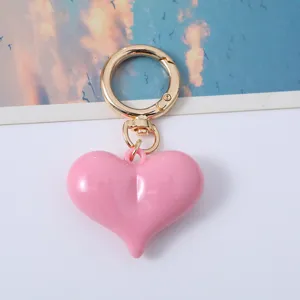 Close-up of a glossy pink acrylic heart-shaped keychain with a polished gold ring.