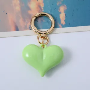 Close-up view of a vibrant lime green acrylic heart-shaped keychain with a polished gold clasp