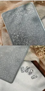 Silver nail art stamping plate with intricate floral designs and finished nail samples.