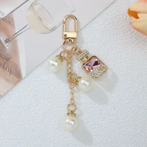 Detalle de llavero dorado elegante con perlas y colgante de frasco de perfume rosa strass