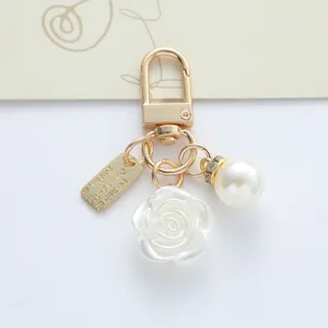 Close-up of gold-plated keychain featuring a delicate white rose and elegant faux pearl bead