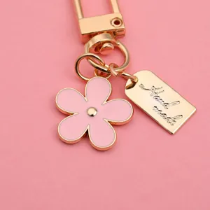 Close-up of pink daisy keychain with gold handmade tag on pink background