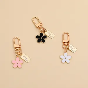 Macro view of three metal daisy keychains in black, pink, and white enamel finishes