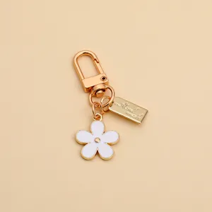 Detailed view of white enamel daisy charm and golden metal keychain hardware