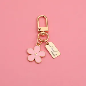 Macro view of pink enamel daisy keychain with gold-plated metal clasp and handmade tag