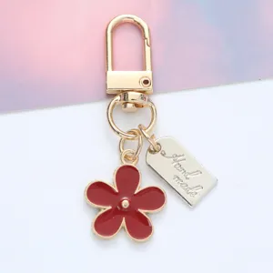 Close-up detail of a red enamel flower keychain featuring a silver Hand made tag