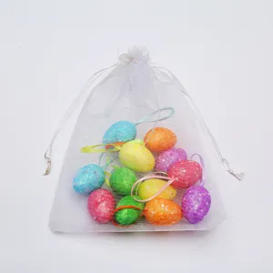 Assorted glittery Easter eggs with hanging strings inside a white mesh drawstring bag