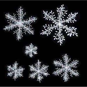 Primer plano de seis adornos de copos de nieve de plástico blanco sobre fondo negro