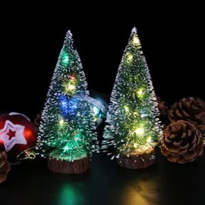 Primer plano de mini árboles de Navidad con luces LED y efecto de nieve sobre base de madera