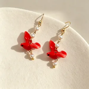 Macro detail of elegant red ceramic bird earrings featuring delicate white pearls