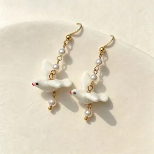 Detailed close-up view of elegant white ceramic bird earrings with delicate pearls.