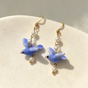 Detailed macro shot of blue ceramic pigeon earrings with pearls and golden hooks