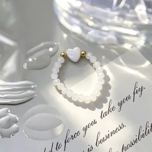 Detailed shot of an elastic beaded ring featuring a white shell heart and gold beads.