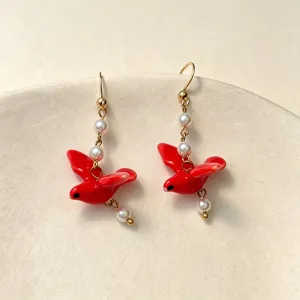 Close-up of vibrant red ceramic bird earrings with pearls and stainless steel hooks