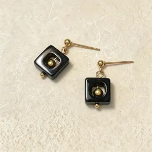 Detailansicht geometrischer schwarzer Quadrat-Ohrringe mit einer goldener Perle.