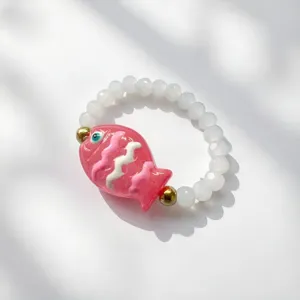 Dettaglio di un ciondolo a forma di pesce rosa su un anello elastico di perline