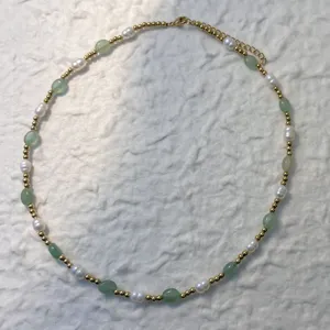 Detail view of natural freshwater pearl and green stone necklace on textured background