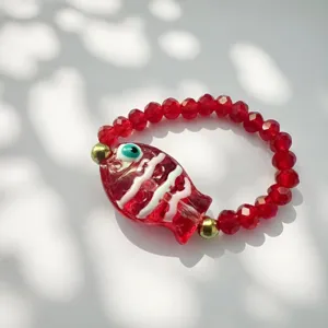 Dettaglio macro di un ciondolo a forma di pesce in vetro rosso su un anello elastico.
