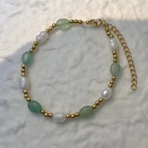 Close-up of a bracelet with natural pearls, green stones, and gold stainless steel beads